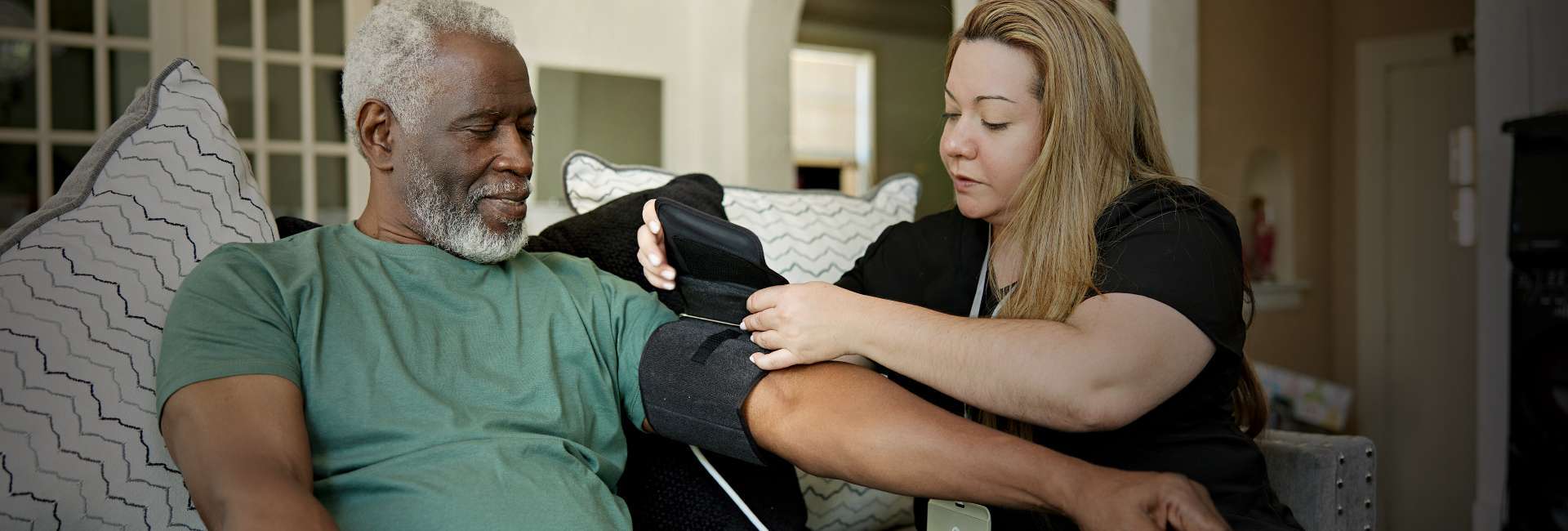 caregiver taking blood pressure for a man wearing a green shirt.